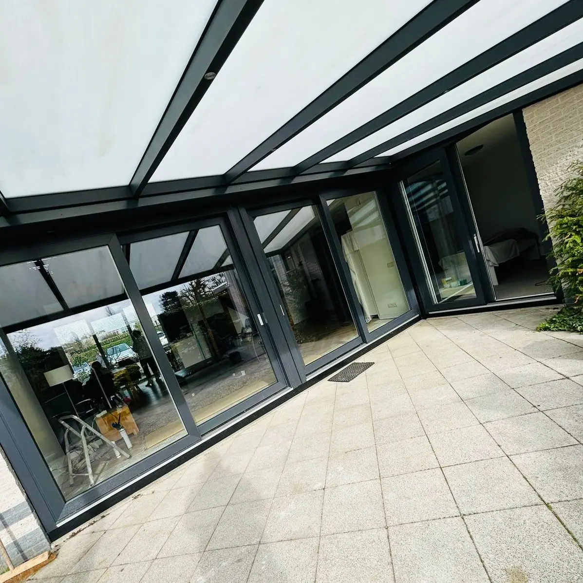 Antraciet kunststof schuifpui onder een overkapping bij een woning met terras.