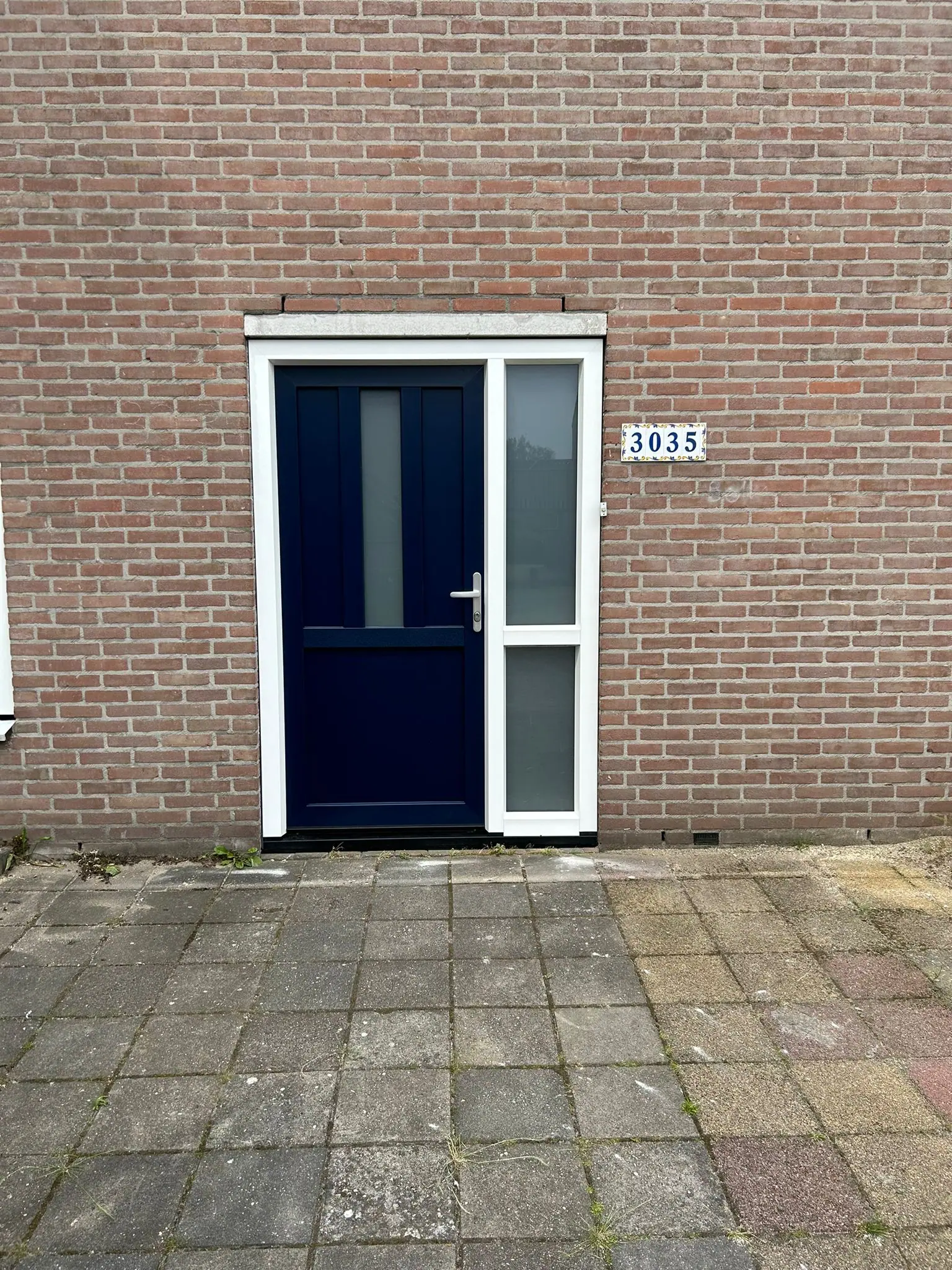 Donkerblauwe kunststof voordeur met wit kozijn en matglas zijlicht bij een bakstenen woning in Hengelo.